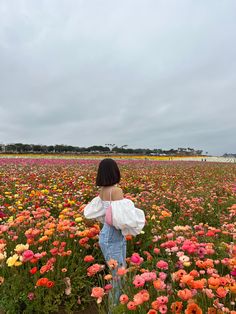 a woman standing in a field full of flowers looking at the sky with her back to the camera