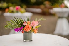 a vase filled with flowers sitting on top of a white table next to tables and chairs