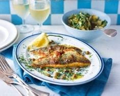 a white plate topped with fish next to two glasses of wine