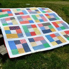 a patchwork quilt sitting on top of a wooden bench in the middle of a field