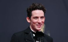 a man in a tuxedo and bow tie smiles for the camera at an event