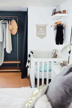 a baby's room with clothes hanging on the wall and a crib in the foreground