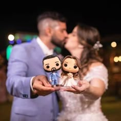 a bride and groom kiss as they hold their wedding cake toppers