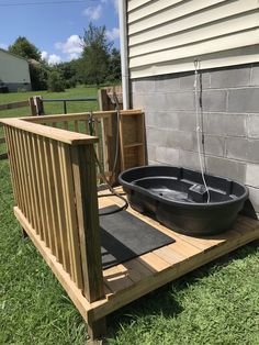 a hot tub on a wooden deck in front of a brick wall and green grass