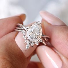 a woman's hand holding an engagement ring with a pear shaped diamond on it