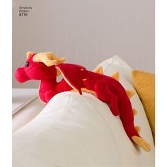 a red stuffed dragon laying on top of a white pillow