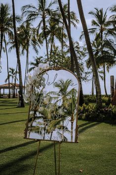 a sign that is sitting in the grass near some palm trees and flowers on it