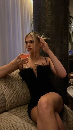 a woman sitting on top of a couch holding a drink