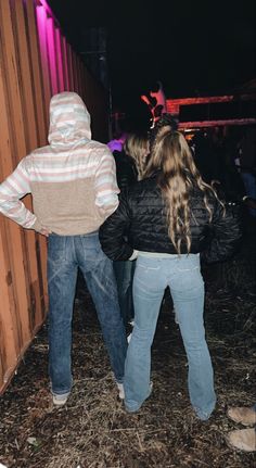 two people standing next to each other in front of a wooden fence at night time