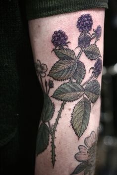 a close up of a person's arm with tattoos on it and purple flowers