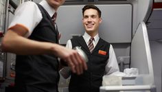 two men are standing in an airplane cabin and one is smiling at the camera man