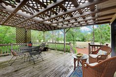 an outdoor deck with wicker chairs and table on it, surrounded by wooded area