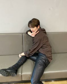 a young man sitting on top of a gray couch next to a wooden floor in front of a white wall