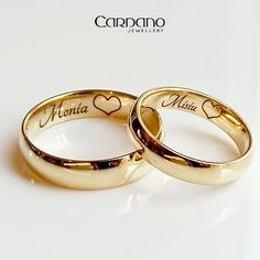 two gold wedding rings with hearts and names on them, sitting next to each other