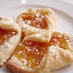 four small pastries on a white plate with powdered sugar and jelly toppings