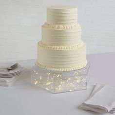 a three tiered white cake sitting on top of a table next to silverware