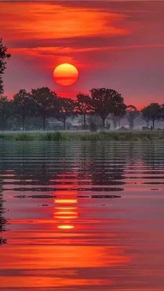 the sun is setting over water with trees in the background