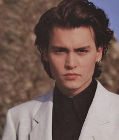 a young man in a white suit and black shirt looking at the camera with an intense look on his face