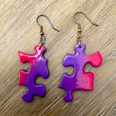 two pieces of purple and pink puzzle piece dangle earrings on a wooden table top