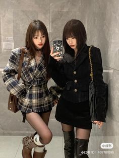 two young women standing next to each other in front of a wall holding up their cell phones