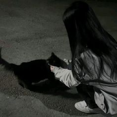 a woman is petting a black cat on the ground in the dark with long hair