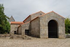 an old stone church with a red roof and two doors on the front is surrounded by trees