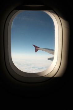 an airplane window looking out at the clouds and blue sky from inside another plane's wing