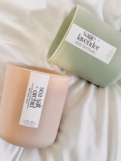 two candles sitting on top of a bed next to each other, one pink and the other green