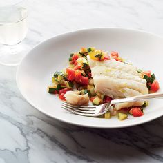 a white plate topped with fish and veggies next to a glass of water