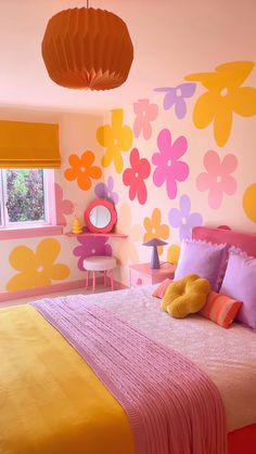 a bedroom decorated in pink, yellow and orange with flowers painted on the wall behind the bed