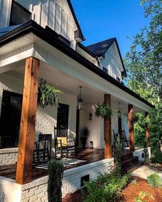 a porch with rocking chairs and plants on the front steps, next to a white brick house