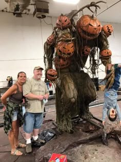 three people standing next to a fake tree with pumpkins on it's head