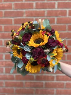 a bridal bouquet with sunflowers and roses in front of a brick wall