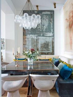 the dining room table is surrounded by white chairs and blue cushions, with an art piece hanging above it