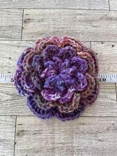 a close up of a crocheted flower on a wooden floor next to a measuring tape