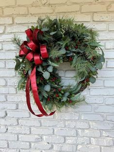 a christmas wreath hanging on the side of a brick wall with a red ribbon around it