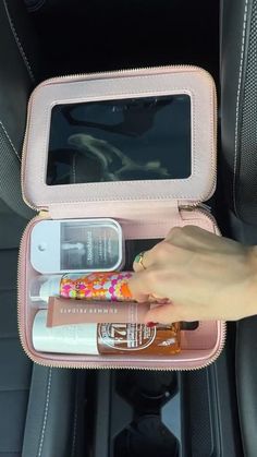 a person holding an open pink case with various items in it on the back seat of a car