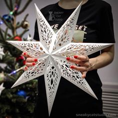 a woman holding a white paper star in front of a christmas tree with decorations on it