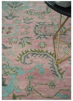 a pink rug with blue and green designs on the floor next to a black table