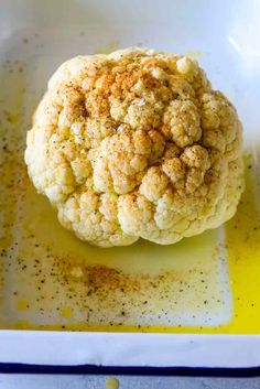 a cauliflower in a white dish with oil and seasoning sprinkles