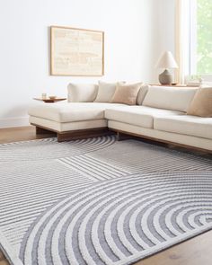 a white couch sitting on top of a wooden floor next to a large gray rug