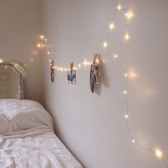 there is a bed with white sheets and string lights on the wall above it, next to a mirror