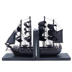 two black ships are sitting side by side on a white background, one has sails and the other has sails down