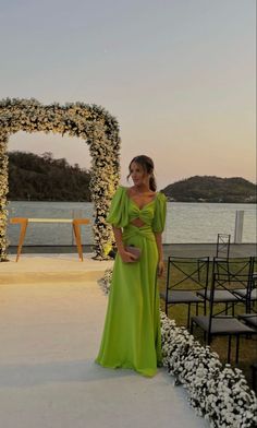 a woman in a green dress standing next to a flower covered archway with flowers on it