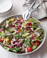 a salad with lettuce, tomatoes and onions in a white bowl on a table