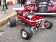 a small red buggy is parked in front of an antique car