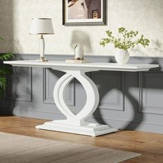 a white table sitting on top of a hard wood floor next to a lamp and potted plant