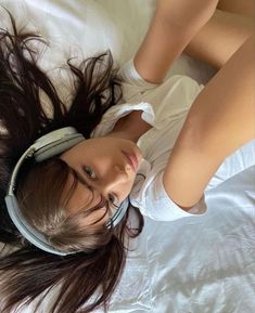 a woman laying on top of a bed with headphones around her neck and hair in the air