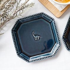 two black plates sitting on top of a table next to a plate with a silver lizard