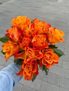 an orange bouquet of flowers in someone's hand on the sidewalk, with brick walkway behind it